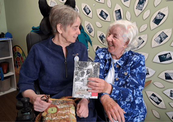 an image of artist Corina Duyn with mentor and artist Caroline Schofield holding a copy of In Bed I Cut Words